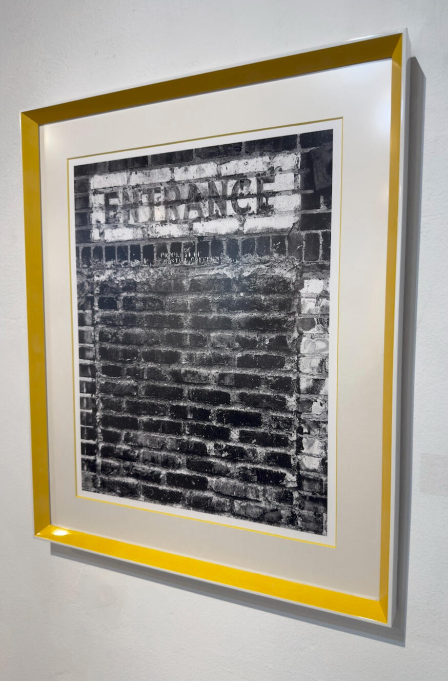 tractor & entrance at TAG Gallery The photograph shows a weathered brick wall with a rectangular sign above.