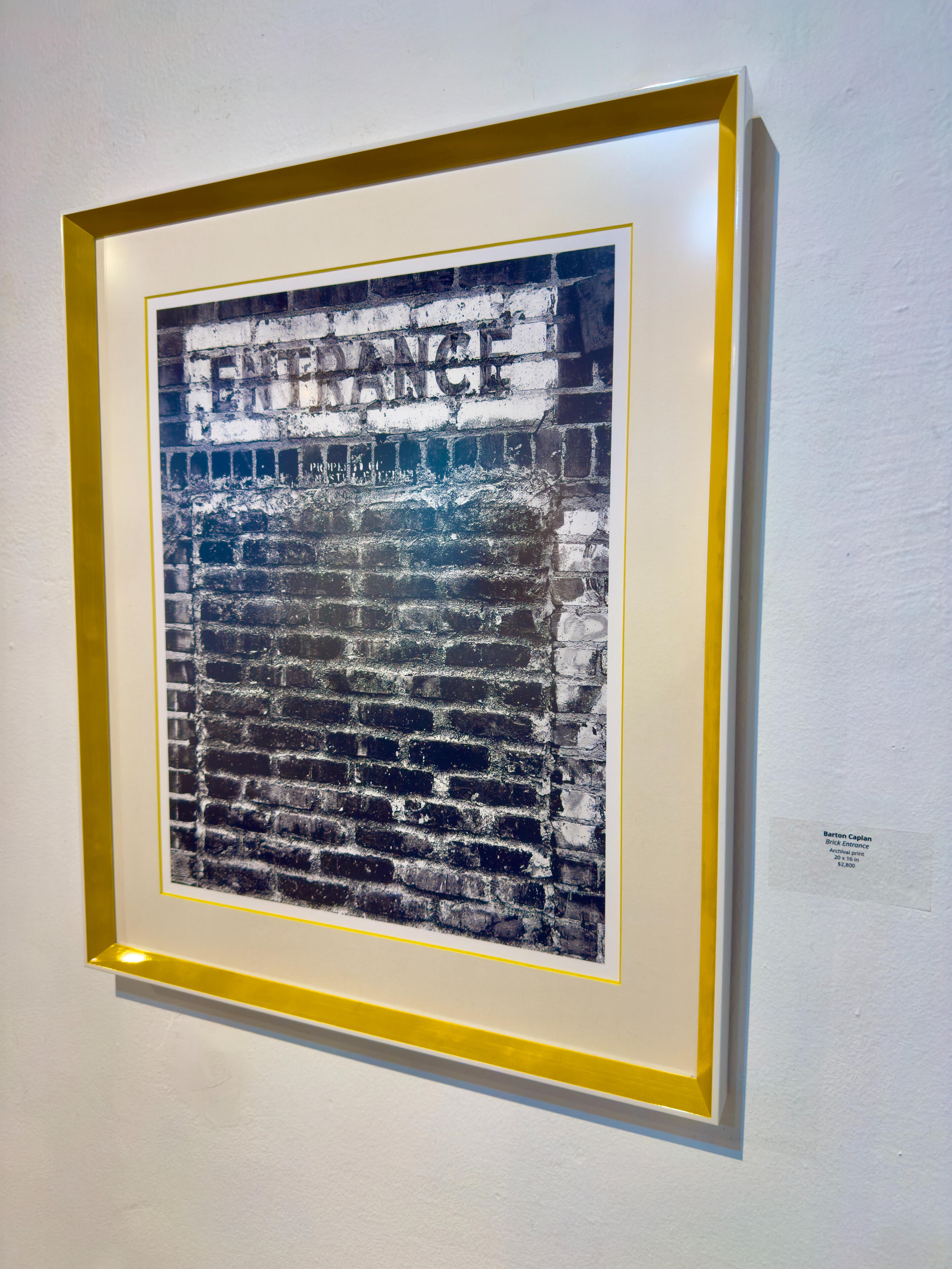 tractor & entrance at TAG Gallery The photograph shows a weathered brick wall with a rectangular sign above.